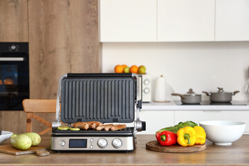 Delicious sausages and vegetables in modern electric grill on table at kitchen