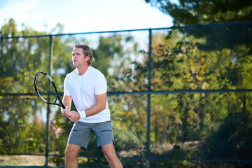 Fototapeta premium A man plays tennis on a court surrounded by trees