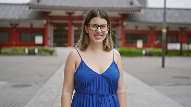 Smiling and joyful, beautiful hispanic woman with glasses posing confidently at the iconic senso-ji shrine in tokyo, exuding natural beauty and carefree happiness