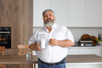 Mature man with filter jug and glass of fresh water in kitchen