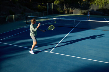 Fototapeta premium A man with long hair plays tennis on a court surrounded by trees