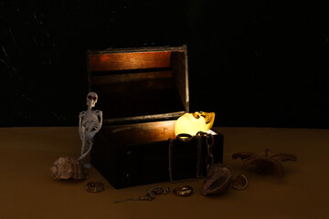 Old chest with treasures, seashells and skeleton on dark background