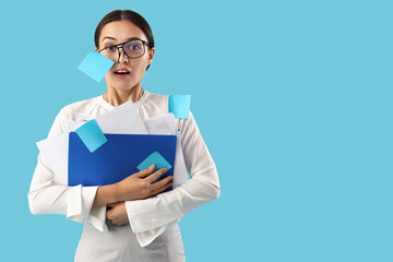 Stressed Asian businesswoman with sticky notes and document folders on blue background
