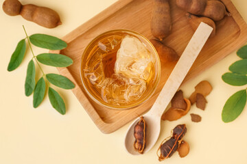 Glass of tasty tamarind drink and fruits on yellow background