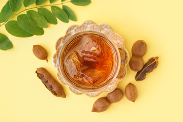 Glass of tasty tamarind drink and fruits on yellow background