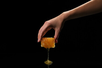 Female hand with sweet honeycomb on black background