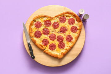 Wooden board with tasty heart shaped pizza on lilac background
