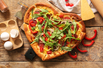 Board with tasty heart shaped pizza and ingredients on wooden background