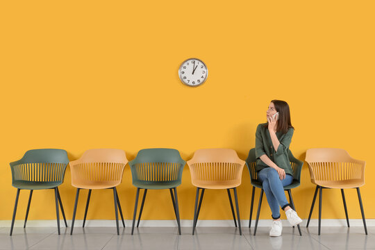 Female applicant with mobile phone waiting for job interview near yellow wall in room
