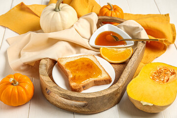 Plate of toast with sweet pumpkin jam and orange on white wooden background