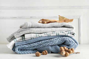 Autumn composition with stack of stylish sweaters and acorns on light background