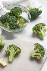 Glass bowl and board with fresh broccoli cabbages on white background