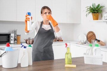 Displeased female janitor with air freshener covering nose in kitchen
