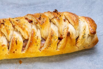 Pizza braid. Delicious braided pizza bread stuffed with cheese, bacon, ham and tomato or barbecue sauce on white baking paper.