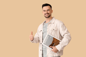 Handsome man with magazine showing thumb-up on beige background