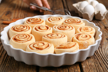 Baking dish with uncooked cinnamon rolls on wooden background