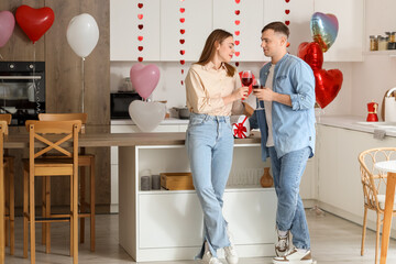 Fototapeta premium Beautiful young couple drinking wine and celebrating Valentine's Day in kitchen at home