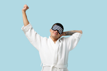 Portrait of handsome young man in bathrobe and sleeping mask on blue background