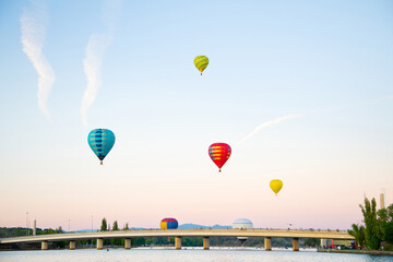 Colorful hot air balloons in sky flying over lake and bridge in Australia.