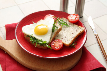 Plate with tasty fried egg, toasts, tomatoes and arugula on light tile background, closeup