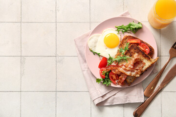 Plate with tasty fried egg, toasts, bacon, tomatoes and glass of juice on light tile background