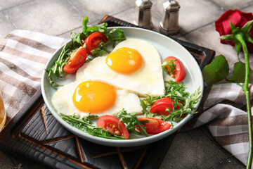Plate with tasty fried eggs, tomatoes, arugula and rose flower on grey tile background, closeup