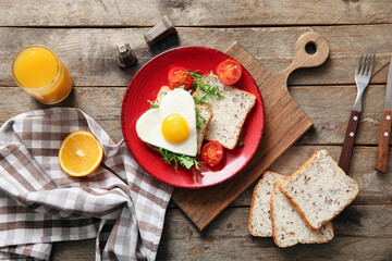 Plate with tasty fried egg, toasts, tomatoes and glass of juice on wooden background