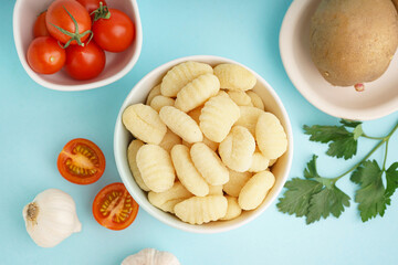 Bowl with tasty gnocchi, garlic and tomatoes on blue background, closeup