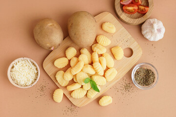 Wooden board with tasty gnocchi, spices and tomatoes on beige background