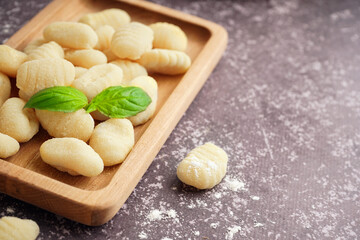 Wooden board with tasty gnocchi and basil on grunge background, closeup