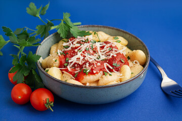 Bowl of tasty gnocchi with tomato sauce and cheese on blue background