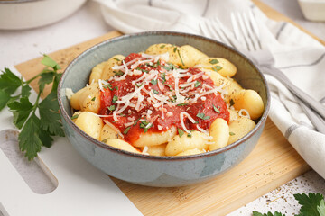 Bowl of tasty gnocchi with tomato sauce and cheese on white background