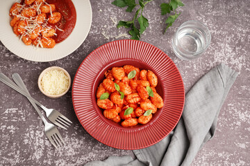 Plates of tasty gnocchi with tomato sauce and cheese on grey background