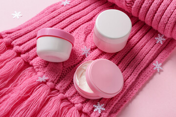 Obraz na płótnie Canvas Jars of cream with decorative snowflakes and warm winter scarf on pink background