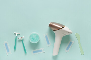 Modern photoepilator with jar of scrub, wax strips and razors on turquoise background
