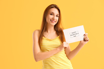 Fototapeta na wymiar Beautiful young woman holding greeting card with text HAPPY VALENTINE'S DAY on yellow background