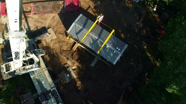 Construction site using crane to move metal container modular home by workers
