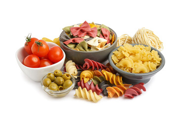 Bowls with different uncooked pasta, tomatoes and olives on white background