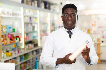 Obraz premium Male pharmacist standing in salesroom of drugstore and demonstrating haircare product