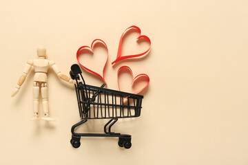 Small shopping cart with wooden human figurine and hearts on beige background. Valentine's Day...
