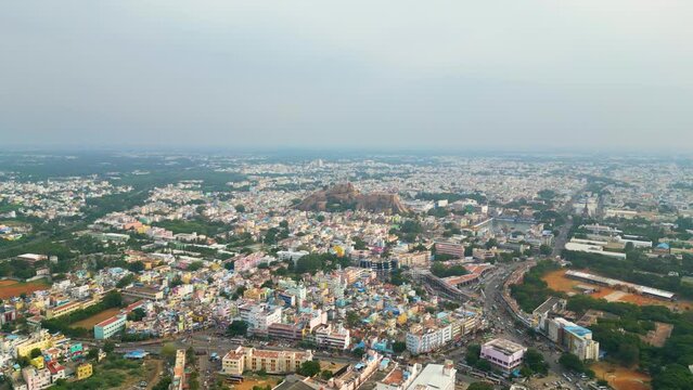 The bustling cityscape of Tiruchirappalli with dense buildings and roads and Malaikottai Rock Fort in the background. Daylight, aerial view. Tamil Nadu, India