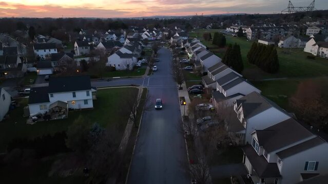 Sunset over American neighborhood. Aerial above street with car at dusk in winter.