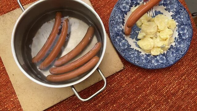 Putting typical German bockwurst sausage on a plate with freshly made potato salad High angle view