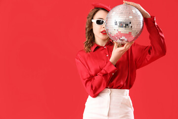 Beautiful young woman in stylish sunglasses with disco ball on red background