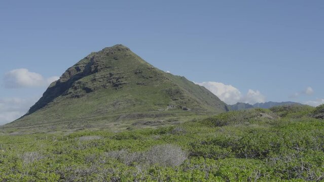 stationary shot of a pointed volcanic mountain on Oahu Hawaii with green lush filds in the foreground and blu sky behind