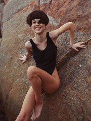 Summer Sensuality: A Gorgeous Bikini-clad Caucasian Woman, Posing on a Rock near a Tranquil Beach Oasis, Radiating Beauty and Happiness in her Sexy Swimwear