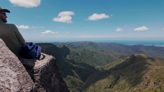 Man sitting on a rock at the top of the mountain range admiring the view. Pinnacles hike, Coromandel Peninsula, New Zealand