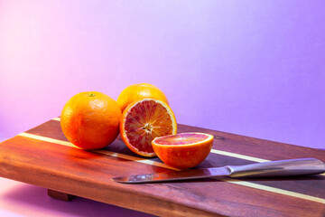 Halved blood oranges on a rustic wooden chopping board next to a knife with impeccable details