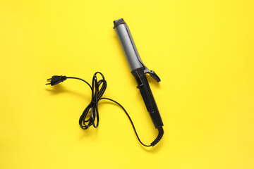 Curling iron on yellow background, top view