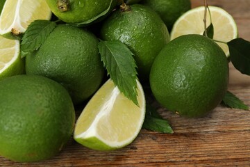 Pile of fresh wet limes and leaves on wooden table, closeup